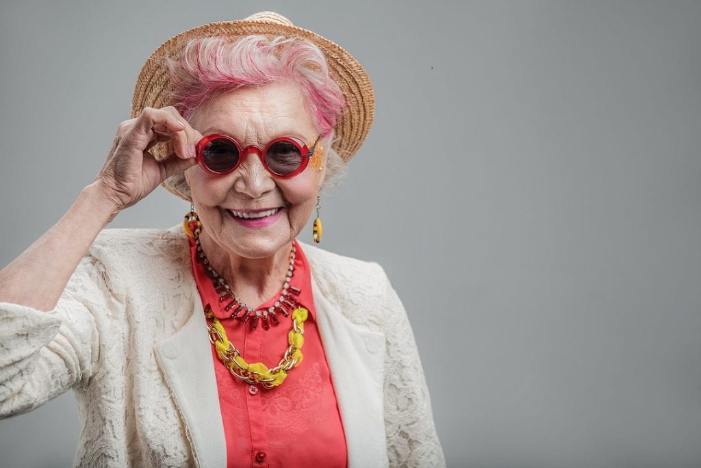 an old lady dressed stylish with pink hair and red sunglasses.she is very happy