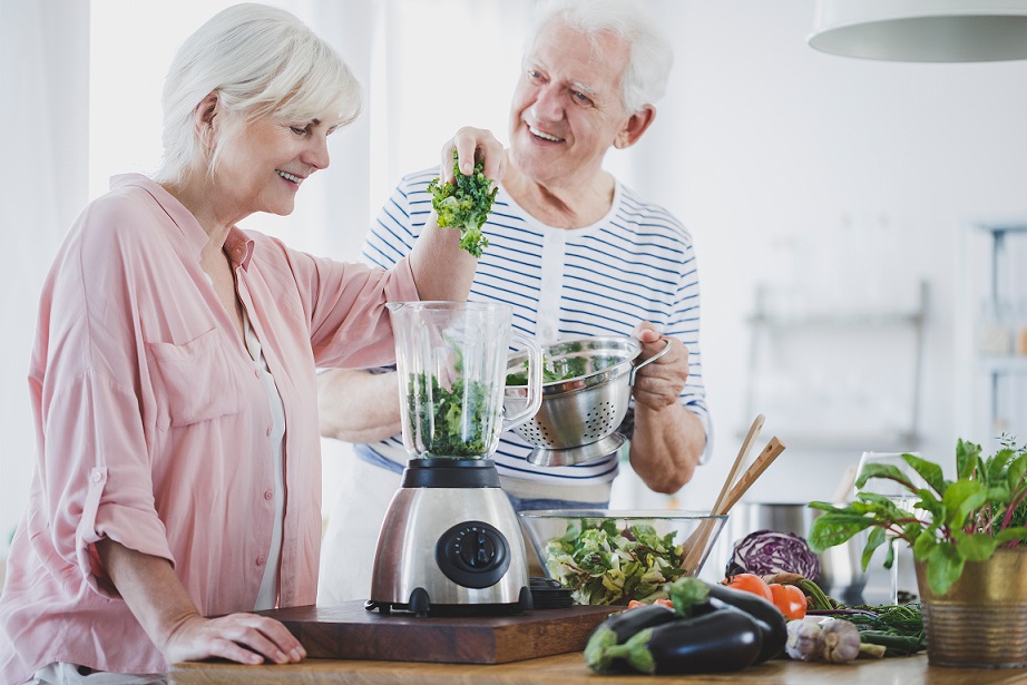 A happy elderly couple blending vegetables in a blender. Vegetarian seniors