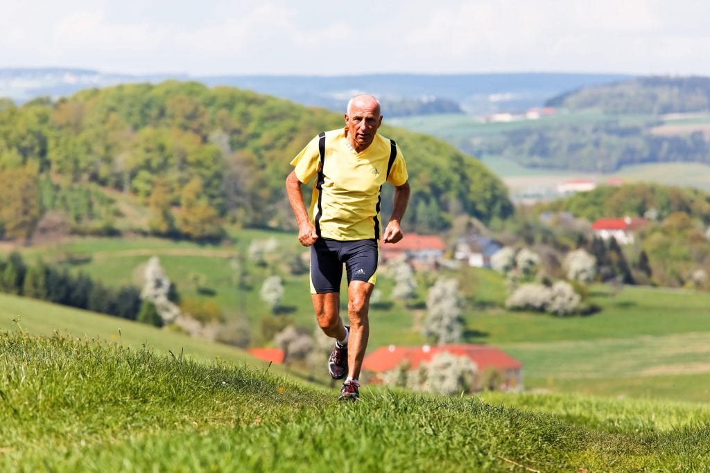 An old athlete man is running up on a hill.