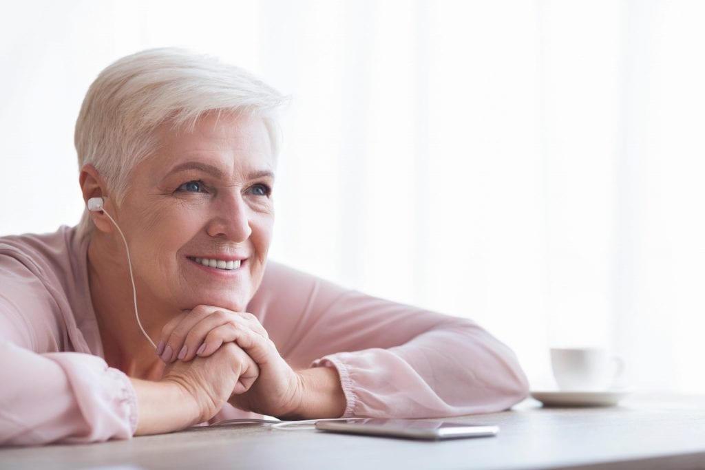 A old woman is listening bye her smartphone to a podcast or music with her headphone.