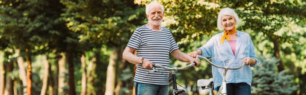 A happy senior couple holding their bicycle in a park.