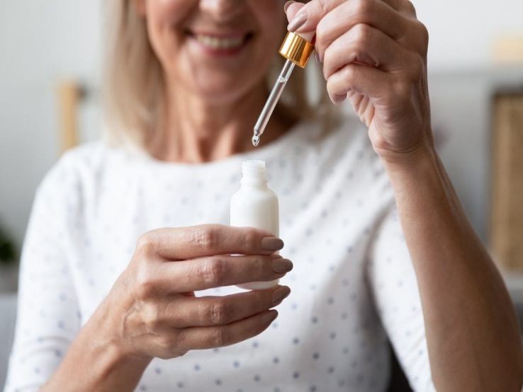 Happy healthy old woman holding face serum bottle in hand ,she is taking care of her skin