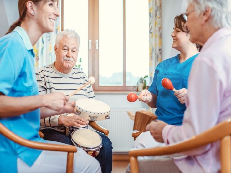 Seniors in the nursing home play music with rhythm musical instruments with the help of caregivers, as a music therapy session.
