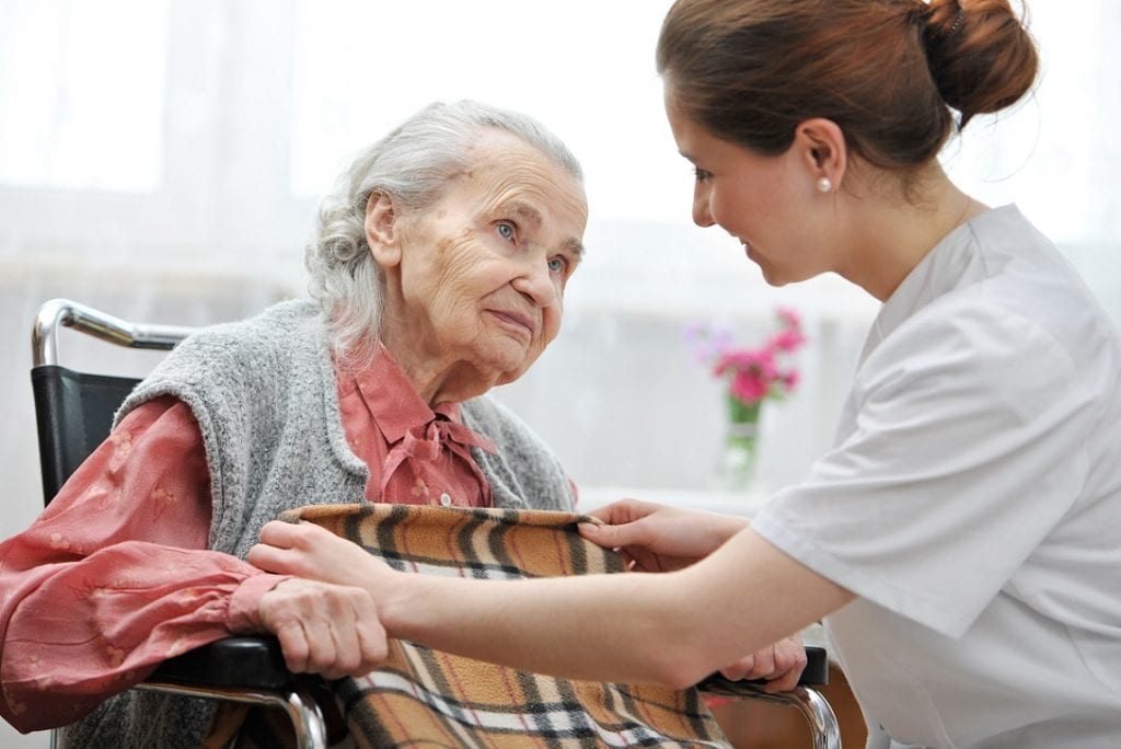 Female nurse helping an old lady  and covers her with a blanket in a nursing retirement home 

