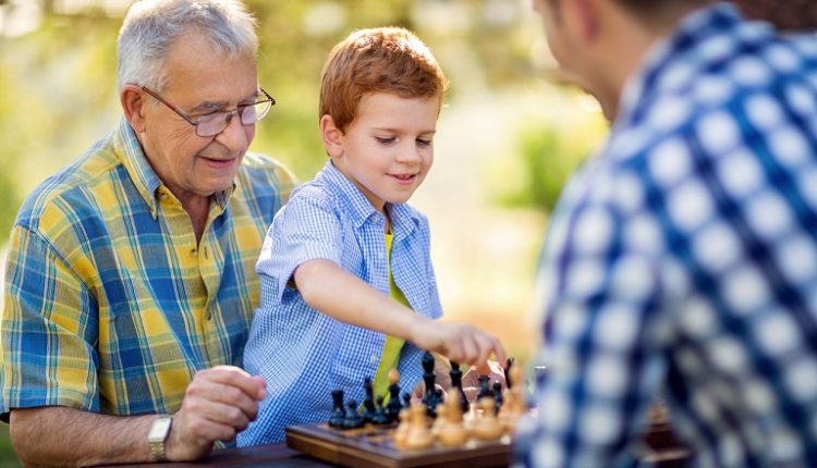 Grandfather, grandson and father are playing chess.