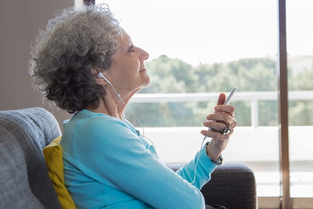 a relaxed older woman wearing earphones enjoying music.  Music therapy concept