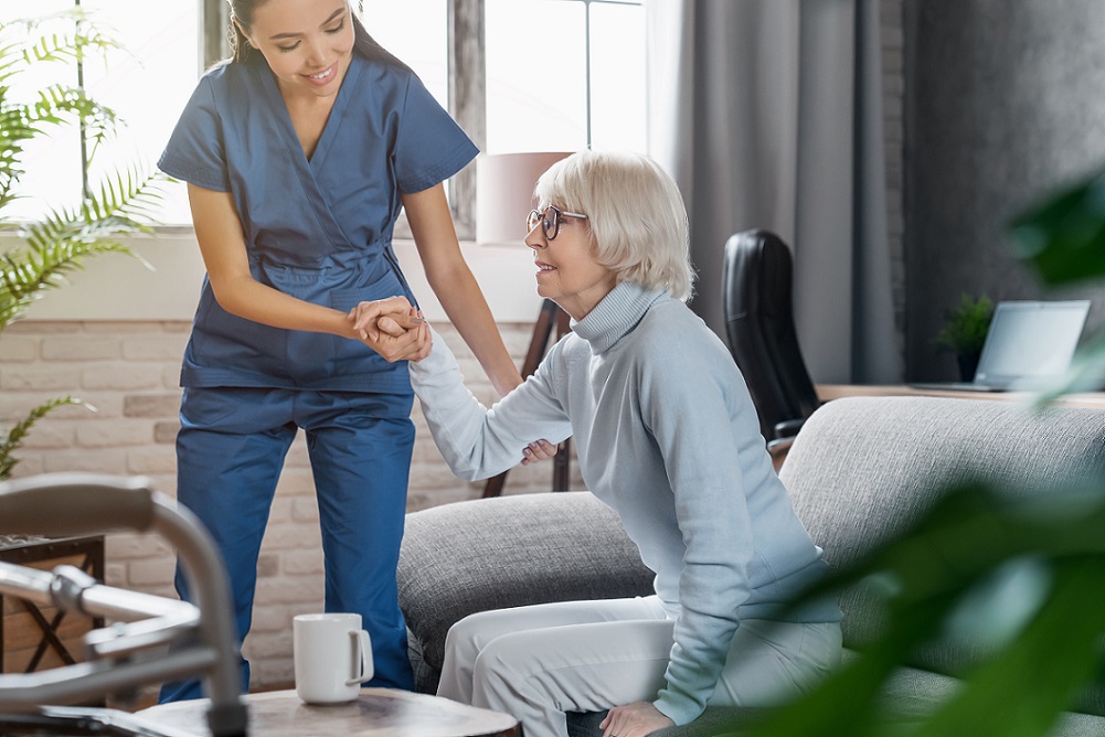 Female nurse is taking care of the senior woman and helping her to stand up.