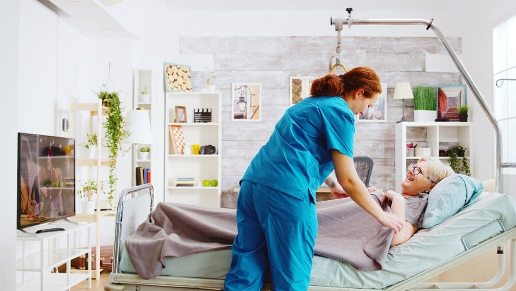 Caregiver is helping senior woman to sleep in bed. 