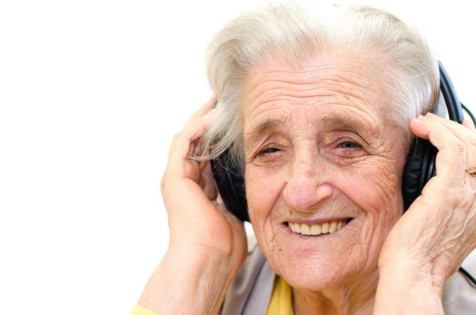 A senior woman listening to music with a headphone. She is smiling.