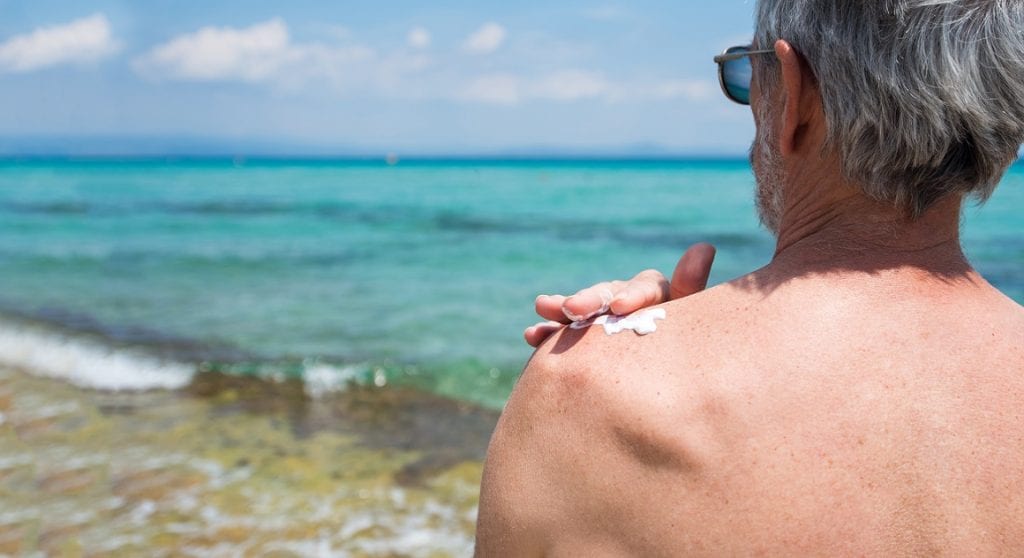Senior man apply sunscreen on his shoulder to take care of his skin
