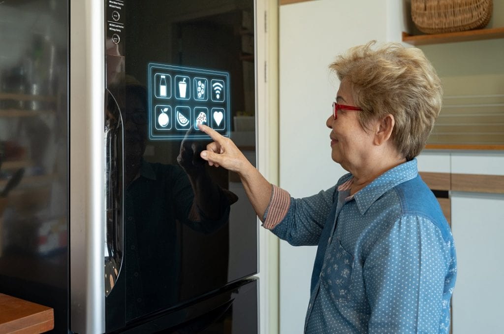 A senior asian woman is touching control panel of display on smart refrigerator.
