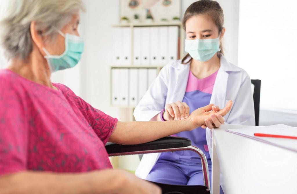 Asian caregiver is checking a senior woman's hand pulse,both wear facial mask for corona.