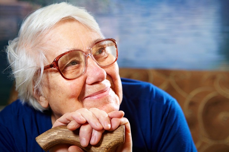 Senior Woman is holiding her cane and smiling. she wears glasses.