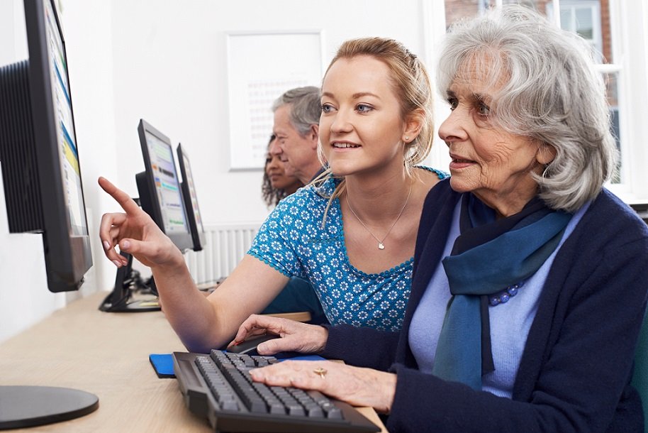 Senior woman is learning using computer from a young student.