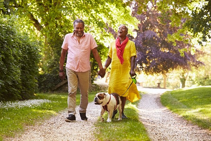 Senior Couple Walking With Bulldog In Countryside. they are laughing.