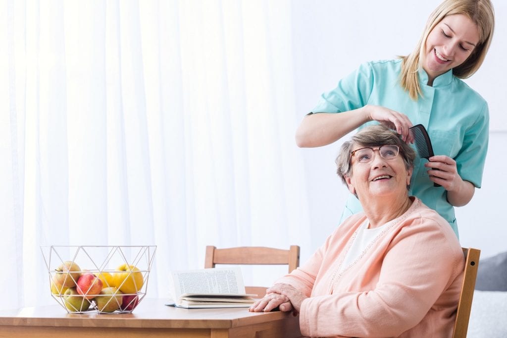 Caregiver communicating with an elderly while combing her hair