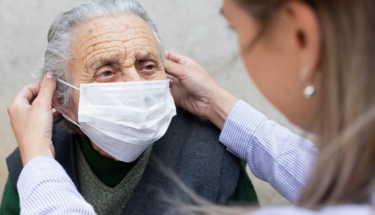 Nurse putting on surgical mask on elderly ill woman - coronavirus protective protocol