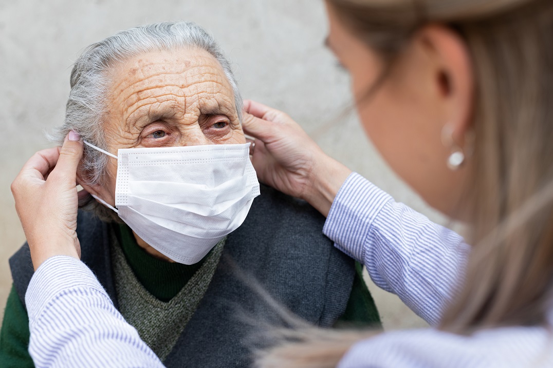 Nurse putting on surgical mask on elderly ill woman - coronavirus protective protocol