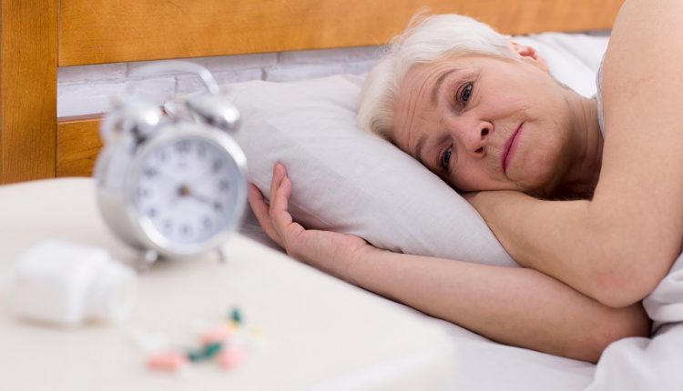 Upset senior lady with sleep disorder lying in bed, pills not helping