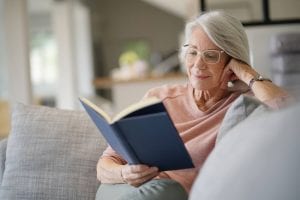 a senior woman sitting on a sofa and reading a book