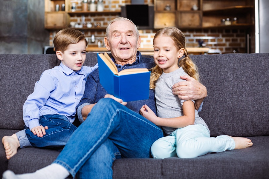 An elderly is reading a book to his grandchildren