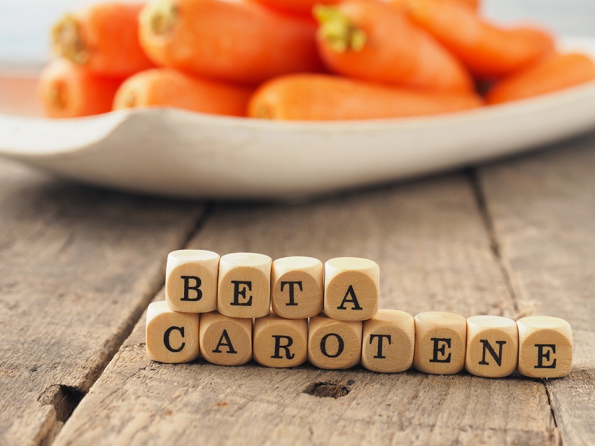 Wooden dices with the words beta carotene and fresh carrots in the back