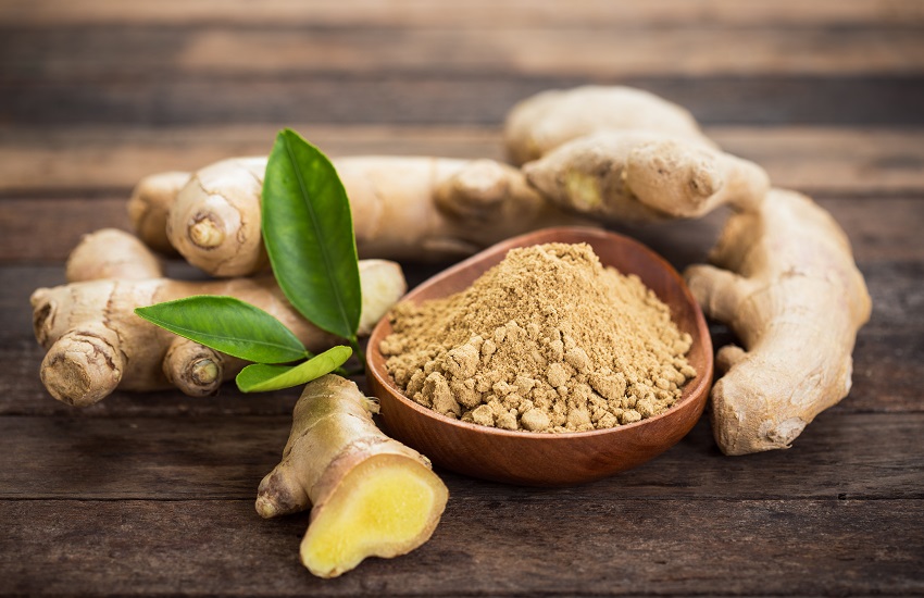 a bowl of ginger powder beside its plant on a wooden table
