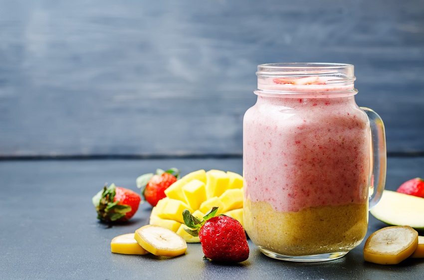 A glass of mango and strawberry smoothie beside fruit pieces