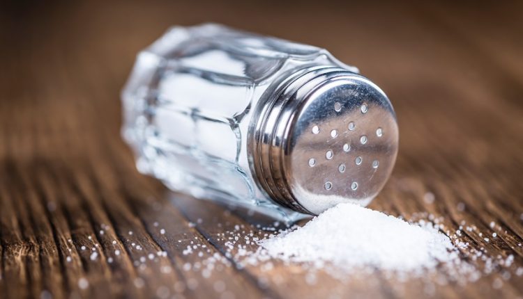 close-up of a salt shaker on a wooden table and some salt spilled on the table