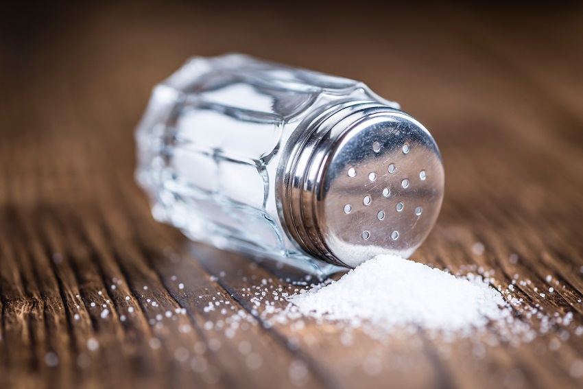 close-up of a salt shaker on a wooden table and some salt spilled on the table