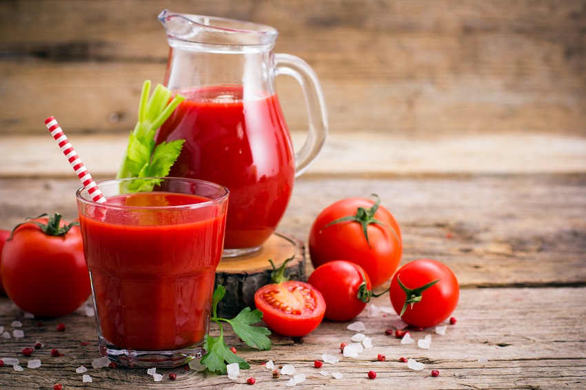 A pitcher and a glass of tomato juice beside a few tomatoes
