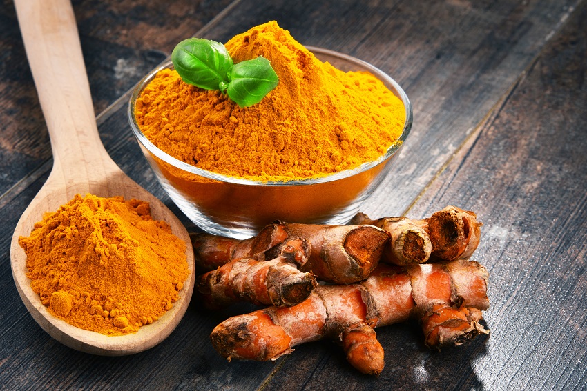 A bowl of turmeric beside a few turmeric plants