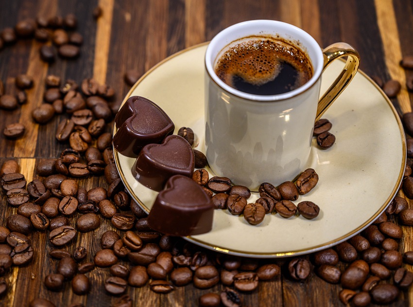 a cup of coffee besides some coffee beans and chocolates