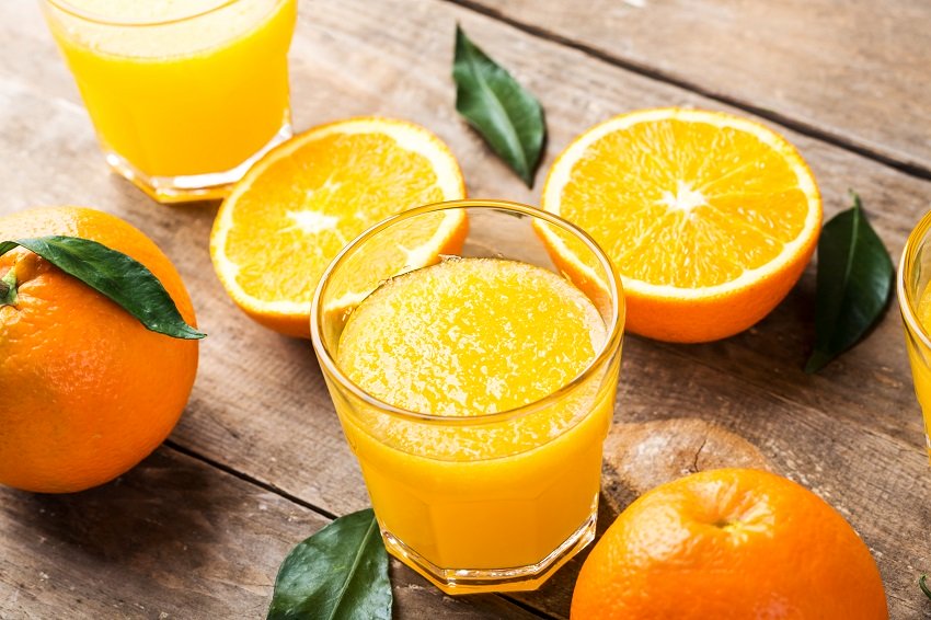 a glass of orange juice beside an orange split in half