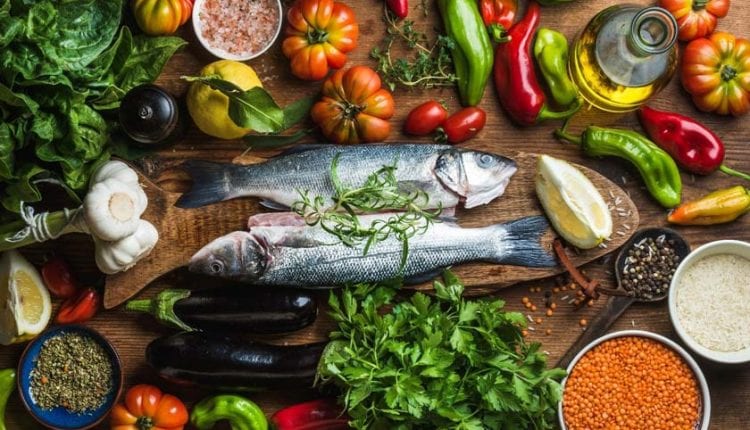 Raw uncooked seabass fish with vegetables, grains, herbs and spices on chopping board over rustic wooden background