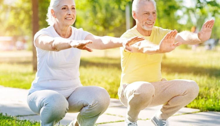 Positive aged couple doing squats in the park.