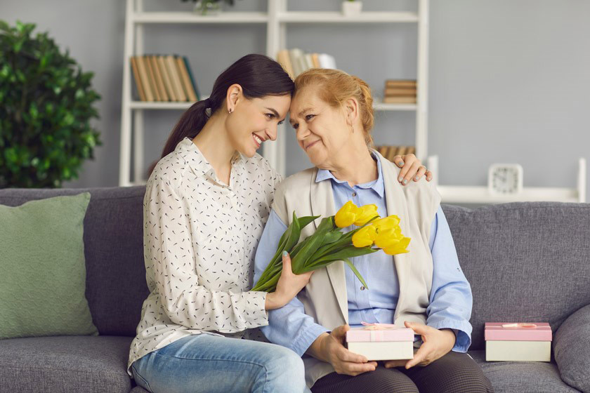 young daughter hugs and gives flowers and gifts to her mature mother