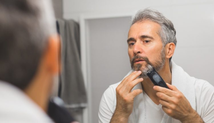 A man shaving his face with an electric razor in front of a mirror