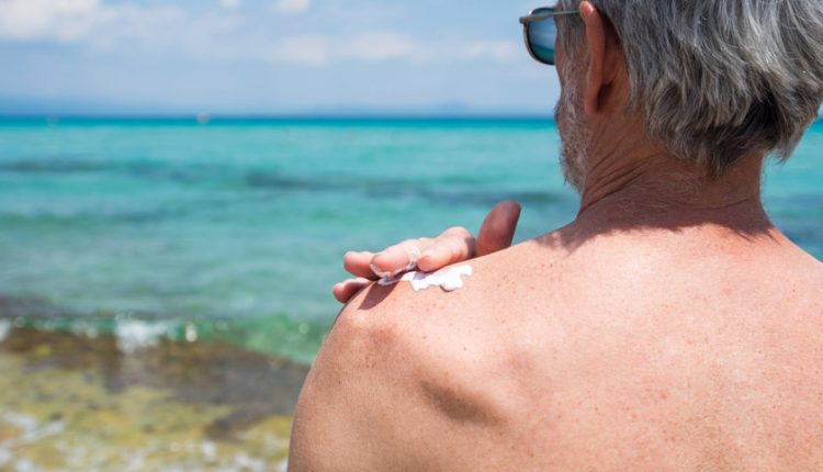 Senior putting sunscreen on his bare shoulder at the beach