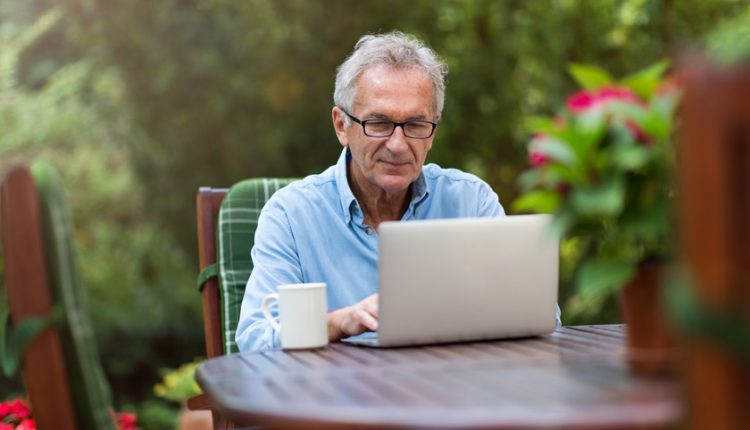 Senior man sitting at a table and blogging with his laptop in the garden