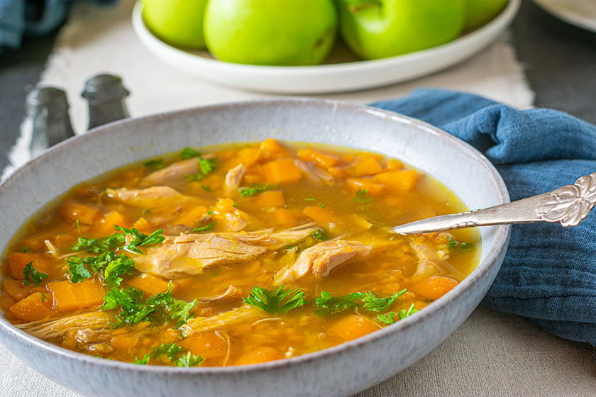 Gluten-free soup with chicken and carrots served on a plate with a spoon on a table.