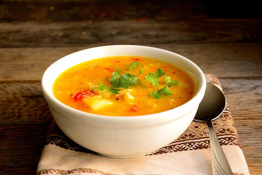 Turmeric vegan soup with vegetables on a wooden table.