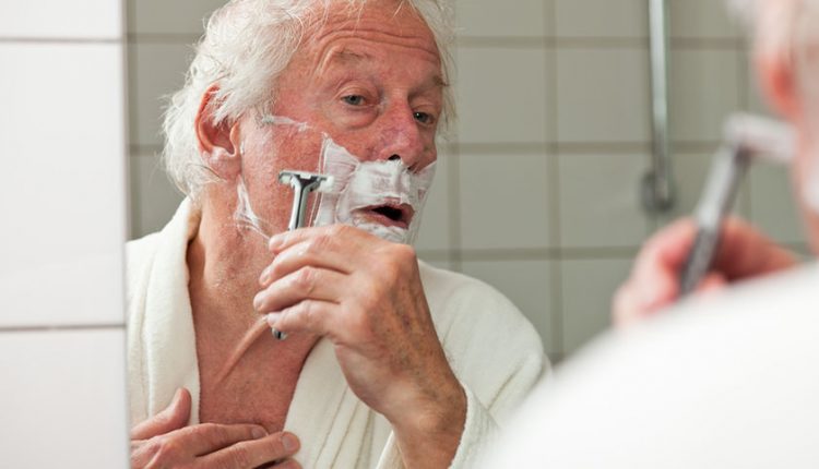 Senior shaving in front of a bathroom mirror