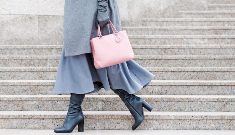 View of a woman in grey with classy boots, leather handbag, and gloves