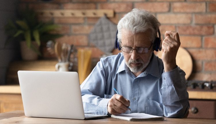 Senior man with headphones concentrating on his studies with a laptop on the desk