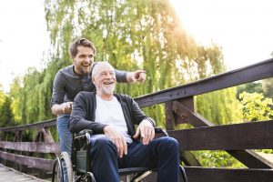 A young man pushing his happy senior father who is sitting on a wheelchair