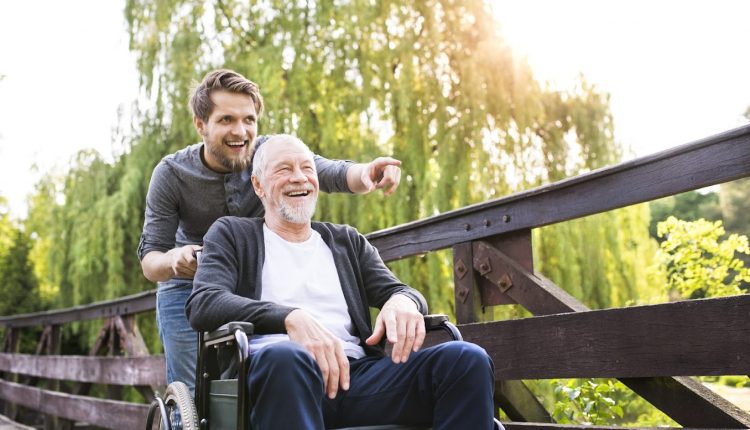 A young man pushing his happy senior father who is sitting on a senior-friendly wheelchair