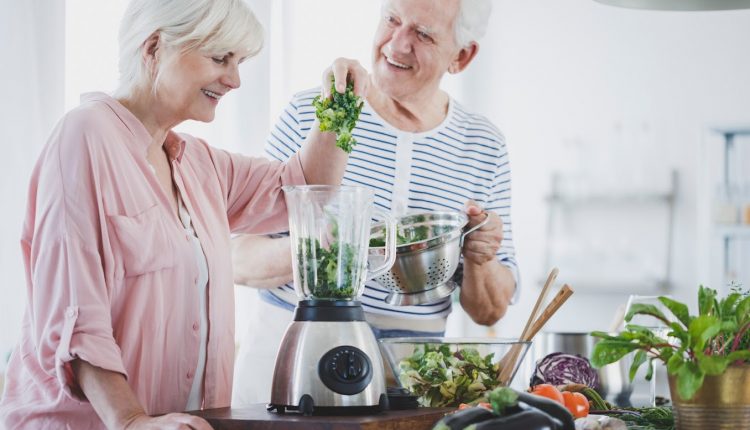 Happy senior couple in their kitchen mixing vegetables in a mixer together in a senior-friendly home