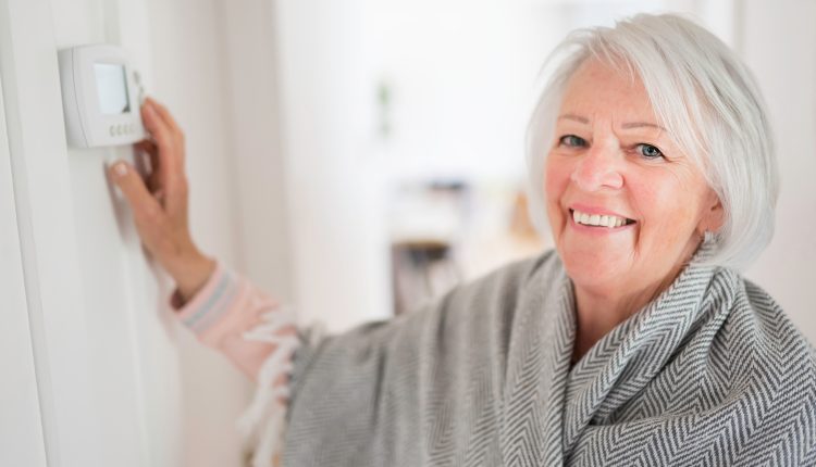 A,Senior,Woman,Adjusting,Her,Thermostat,At,Home