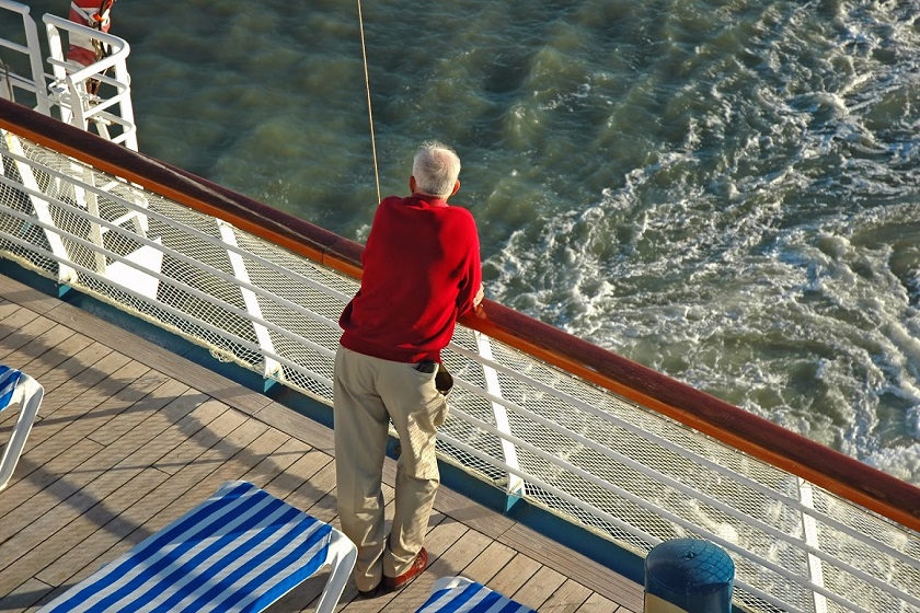 A senior man looks out over the rail of a cruise ship